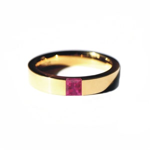 Puede incluir: Un anillo de banda de oro con una piedra preciosa de rubí de forma cuadrada engastada en el centro.