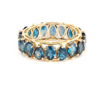 Puede incluir: Un anillo de banda de oro con una fila de piedras preciosas azules en forma de pera.