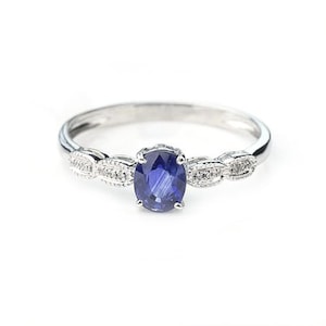 May include: A silver ring with a blue sapphire gemstone and small diamonds set in a delicate, vintage-inspired design.