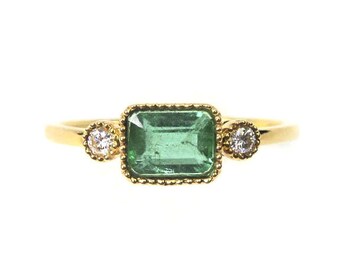 May include: A gold ring with a green emerald gemstone and two smaller diamond accents.