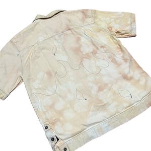 May include: A beige short-sleeved button-down shirt with a bleach-splattered design and black flame outlines.