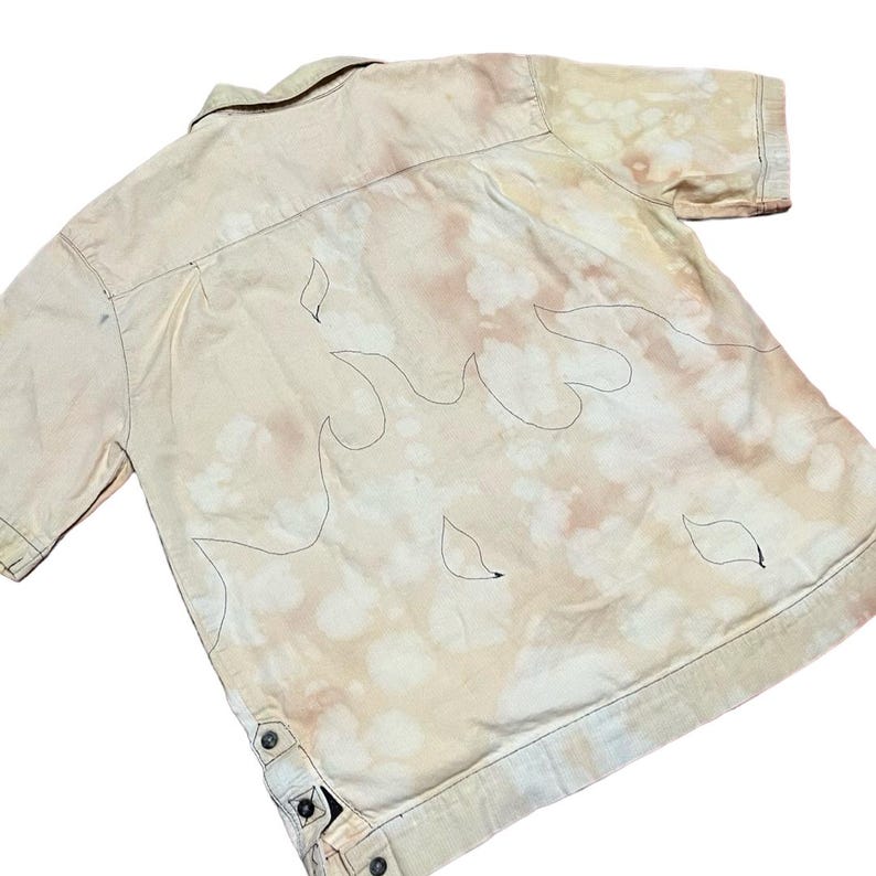May include: A beige short-sleeved button-down shirt with a bleach-splattered design and black flame outlines.