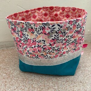 Puede incluir: Una cesta de almacenamiento de tela turquesa con un borde plateado y un forro con estampado floral. La cesta est&aacute; hecha de una tela suave y duradera y es perfecta para organizar art&iacute;culos peque&ntilde;os.