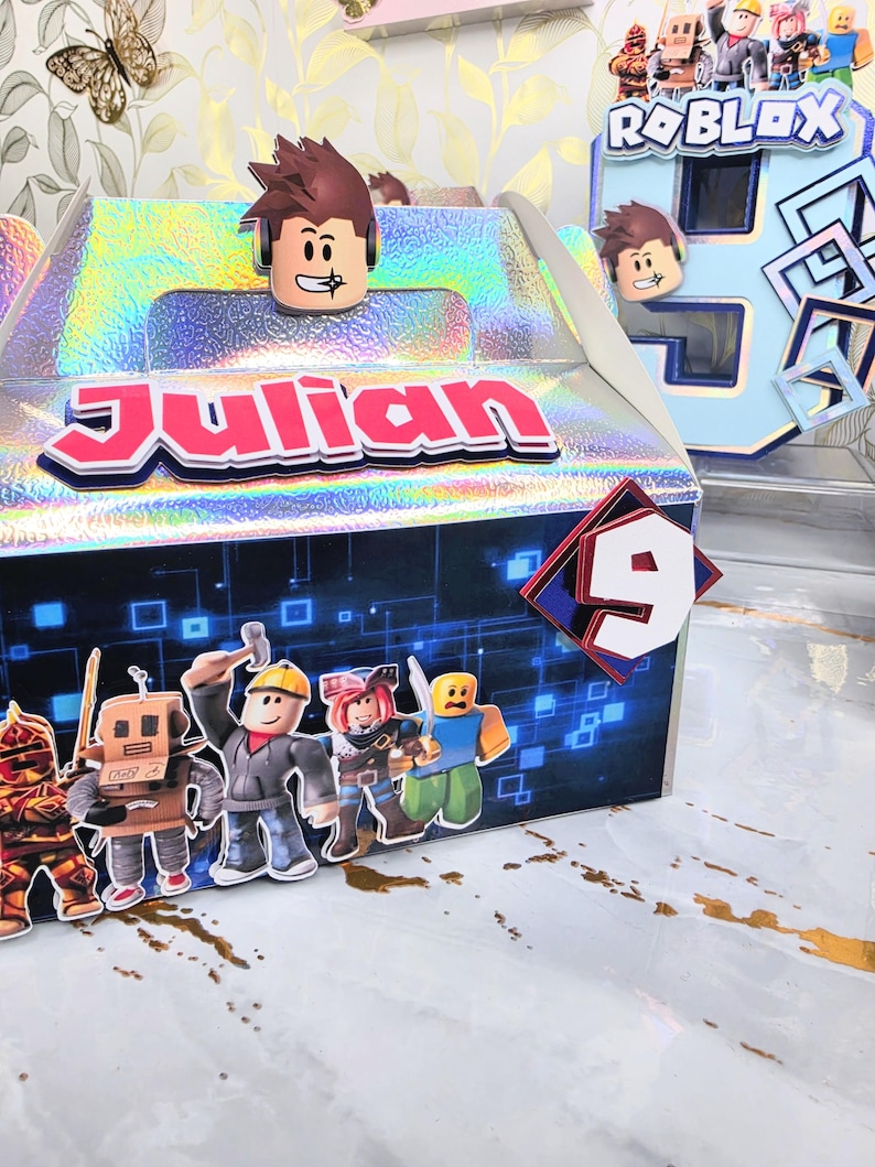 K&ouml;nnte beinhalten: Eine holografische Geschenkbox mit dem Namen "Julian" in roten Buchstaben. Die Box ist mit Roblox-Charakter-Ausschnitten und der Zahl 9 verziert. Im Hintergrund befindet sich eine gro&szlig;e blaue Zahl 6 mit Roblox-Charakteren.