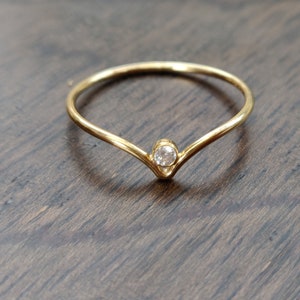 May include: A gold ring with a single, clear gemstone set in a V-shaped band.