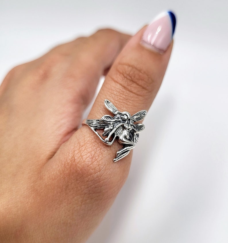 May include: A silver ring featuring a detailed fairy design. The fairy is depicted with wings outstretched and a delicate, intricate design.