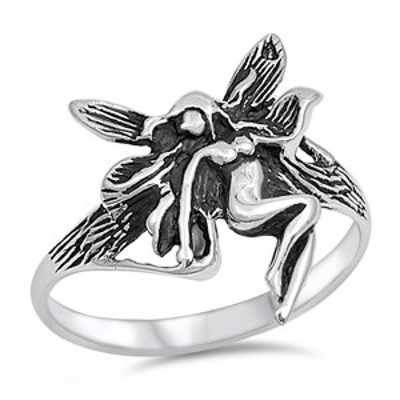 May include: A silver ring featuring a detailed fairy design with wings outstretched. The fairy is depicted in a sitting position with its wings spread wide.