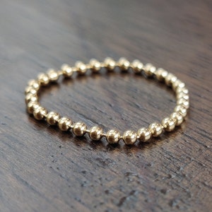 May include: A gold beaded bracelet with a simple design. The bracelet is made of small, round beads that are connected together to form a chain.