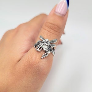 May include: A silver ring featuring a detailed fairy design with outstretched wings.