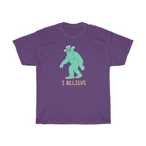 May include: Purple t-shirt with a green monster graphic and the text "I BELIEVE" in pink and blue.