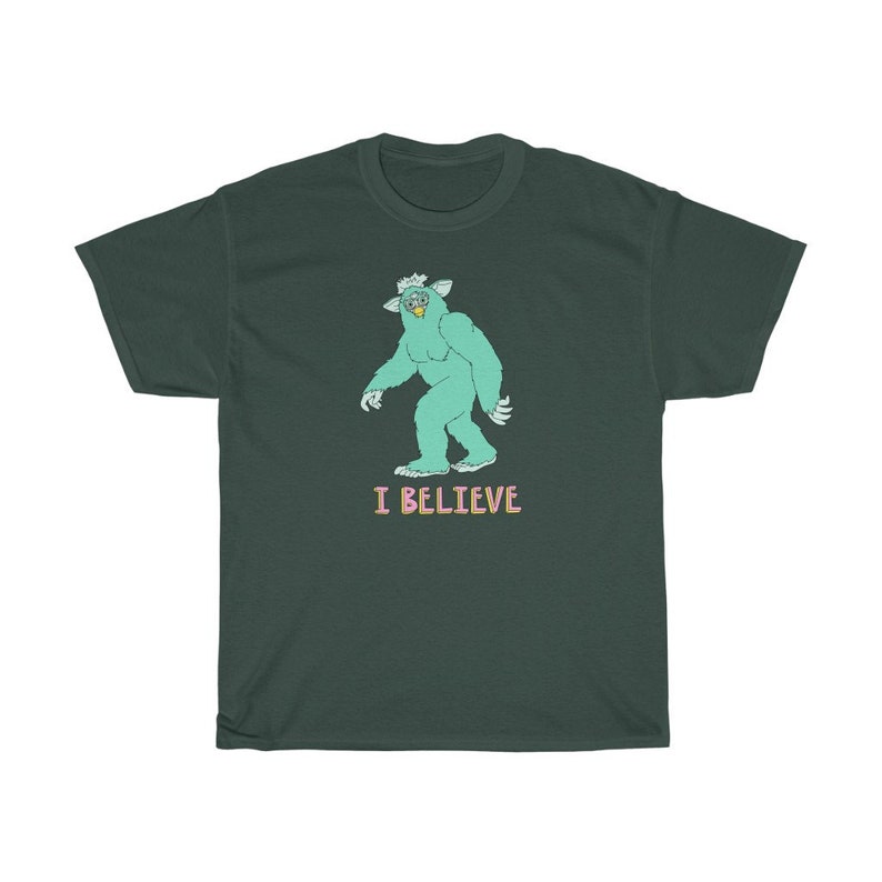 May include: A dark green t-shirt with a cartoon illustration of a green monster with a crown and the text "I BELIEVE" in pink and light blue.