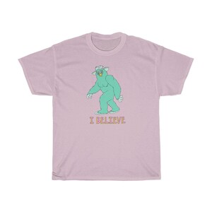 May include: A pink t-shirt with a green monster graphic and the text "I BELIEVE" in pink and yellow.