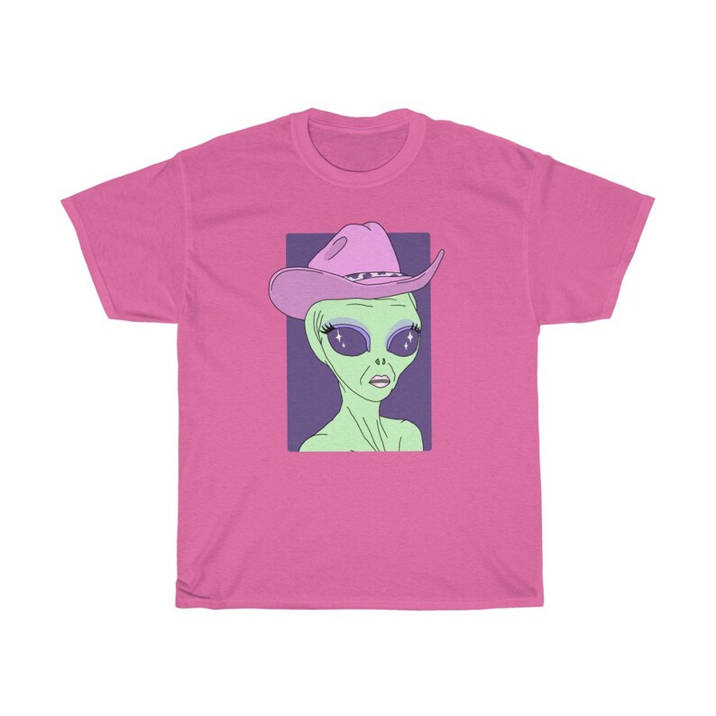 May include: A pink t-shirt with a graphic of a green alien wearing a pink cowboy hat with a purple band. The alien has large, sparkling eyes.