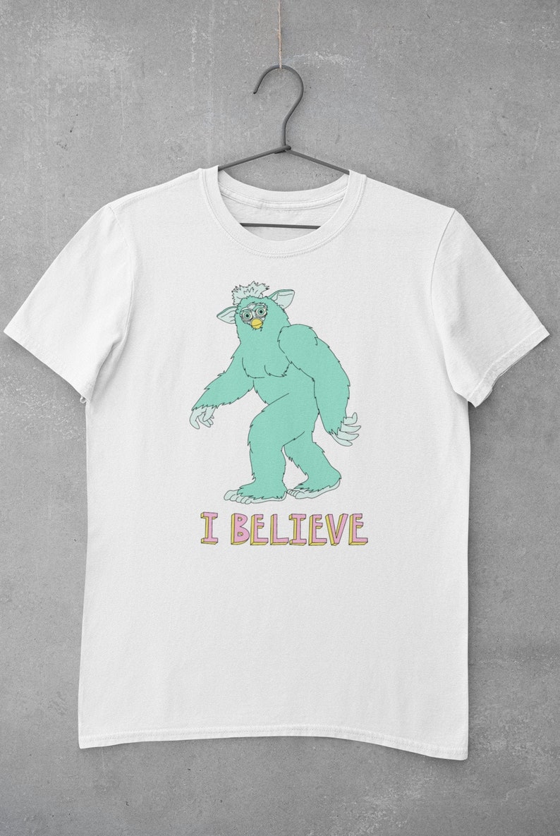 May include: White t-shirt with a cartoon green monster wearing glasses and the text "I BELIEVE" in pink and yellow letters.
