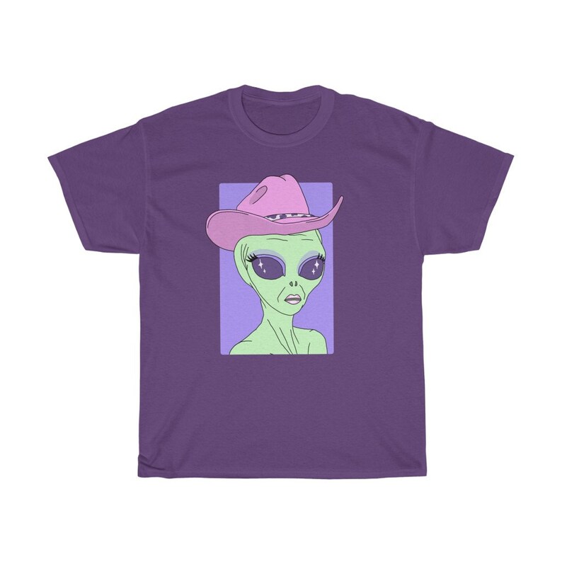 May include: A purple t-shirt with a graphic of an alien wearing a pink cowboy hat with sparkly eyes. The alien is green and has a light purple background.