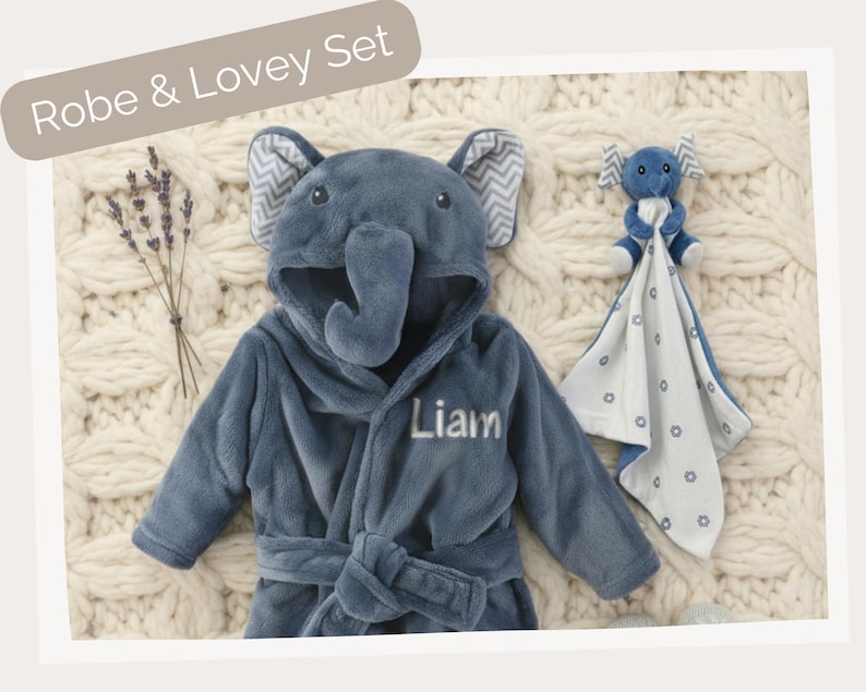 A blue elephant-shaped robe with the name "Liam" printed on it, along with a blue elephant-shaped blanket and a stuffed elephant toy, all arranged on a white knitted blanket.
