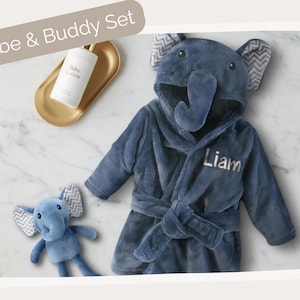 A blue elephant-shaped robe with the name "Liam" written on it, along with a small stuffed elephant toy, is displayed on a marble surface.
