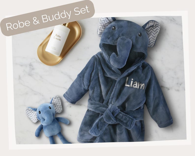 A blue elephant-shaped robe with the name "Liam" written on it, along with a small stuffed elephant toy, is displayed on a marble surface.