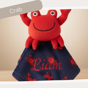 A red plush crab toy with a blue blanket featuring the name "Liam" printed on it.