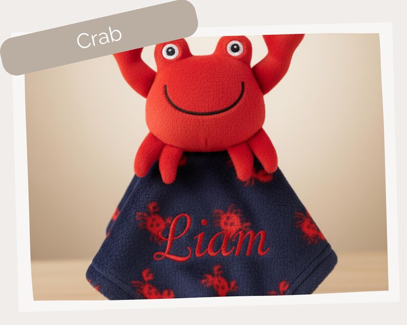 A red plush crab toy with a blue blanket featuring the name "Liam" printed on it.