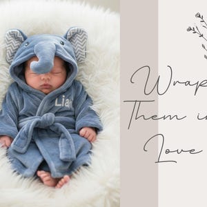 A sleeping baby dressed in a blue elephant-themed robe is pictured on a white fur-covered surface.