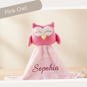 A pink plush owl toy with the name "Sophia" written on it, sitting on a pink blanket.