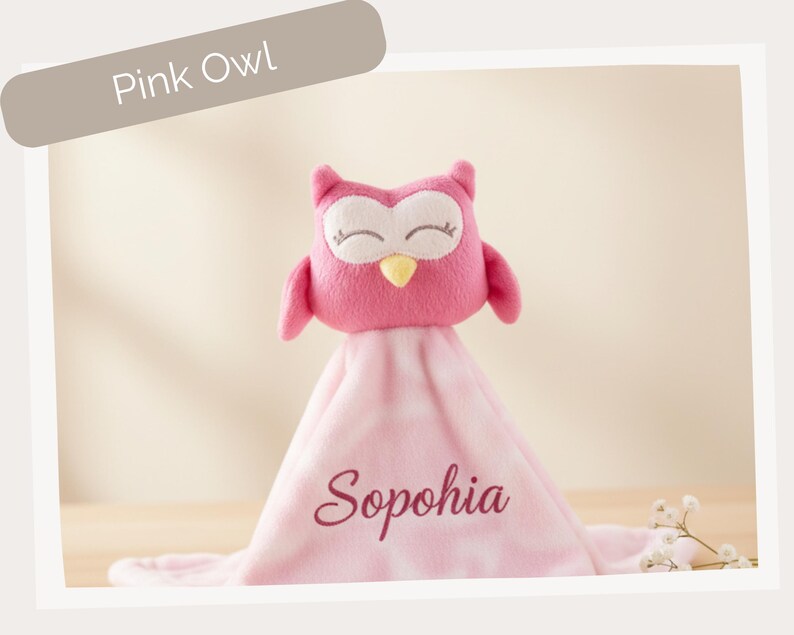 A pink plush owl toy with the name "Sophia" written on it, sitting on a pink blanket.