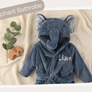 A plush elephant bathrobe with the name "Liam" written on it, along with a wooden elephant toy, is displayed on a beige background.