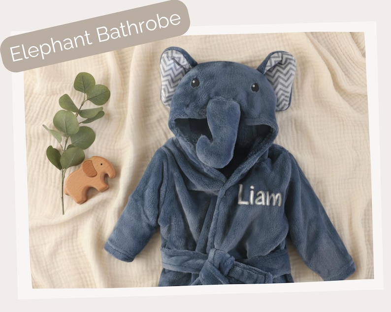 A plush elephant bathrobe with the name "Liam" written on it, along with a wooden elephant toy, is displayed on a beige background.