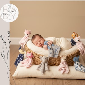A newborn baby is peacefully sleeping in a basket filled with various stuffed animals, including a fox, a giraffe, and a blue elephant.