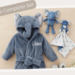 A blue elephant-themed robe with the name "Liam" printed on it, along with two stuffed elephant toys and a white blanket with blue polka dots.