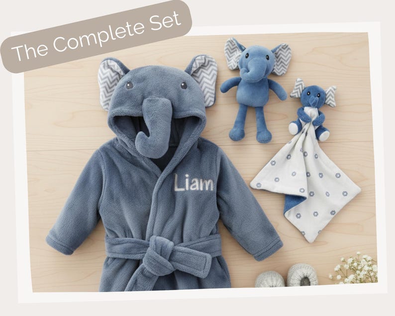 A blue elephant-themed robe with the name "Liam" printed on it, along with two stuffed elephant toys and a white blanket with blue polka dots.