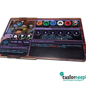 May include: A purple and black board game card with the title "Hijos del Vud&uacute;" and the text "Distrito inicial: PAC&Iacute;FICA". The card has a cost of three gold coins and features a purple and black illustration of three characters. The card also includes a section for activation, recovery, and Netrunners M&iacute;sticos.