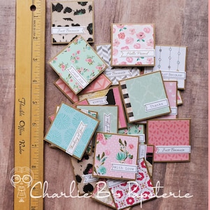 Puede incluir: Una colección de pequeñas tarjetas de felicitación cuadradas con varios diseños florales y estampados. Cada tarjeta tiene un borde marrón y una pancarta blanca con frases como "Just Because" y "With Love".