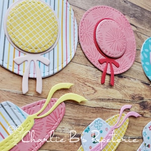 May include: Close-up of several die-cut paper hat shapes in pastel colors. One hat is yellow with a grid pattern, another is pink with a red bow. The hats are on a wooden surface. The text "Charlie B's Papeterie" is visible.
