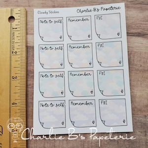 May include: A sheet of stickers with a cloudy sky design. Each sticker has a square shape with a curved corner and a heart symbol. The stickers have the words "Note to self", "Remember", and "FYI". The brand name "Charlie B's Papeterie" is also visible.