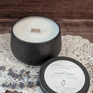 May include: Black candle jar with a wooden wick and a black lid. The lid has a white label with the text "SIMPLE FLOWER STUDIO", "sweet home", "citrus + currant", "SCENTED COCOSOY WAX", "20 hr. burn time", and "4 oz."