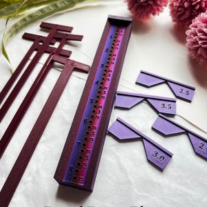 May include: A set of purple and red plastic knitting needles with a ruler and gauge markers. The ruler has markings for 2.5, 3.0, 3.5, and 4.0 mm. The text "Royal Berry Blaze" is printed below the needles. The color pattern you receive will vary due to the fast color-changing gradient filament.