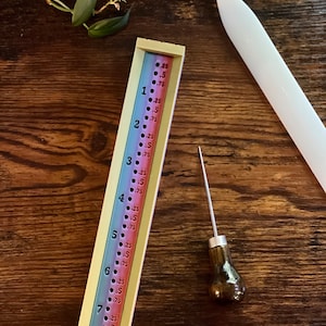 May include: A colorful ruler with markings in inches and fractions of an inch. The ruler is made of plastic and has a white background with colored stripes. The ruler is numbered from 1 to 8. A small awl with a brown wooden handle is also pictured.