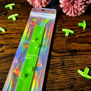 May include: A green plastic ruler with two rows of small, round knobs. The ruler is packaged in a clear, iridescent plastic bag.