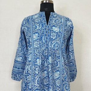 May include: A blue and white floral print cotton tunic top with a V-neck and 3/4 sleeves. The top has a beaded trim along the neckline and a gathered waist.