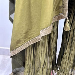 May include: A green, pleated, flowing skirt with a matching green, sheer, embroidered dupatta. The dupatta has a gold trim and a tassel.