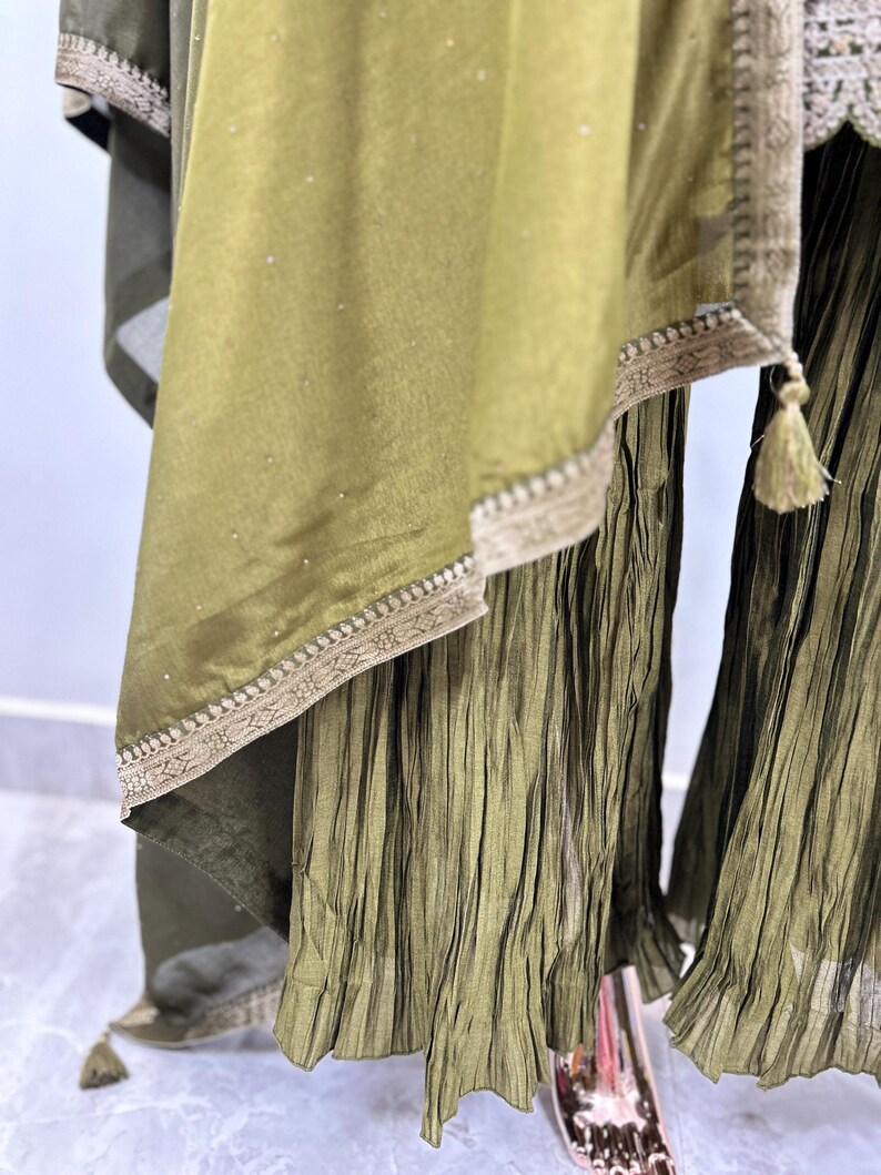 May include: A green, pleated, flowing skirt with a matching green, sheer, embroidered dupatta. The dupatta has a gold trim and a tassel.