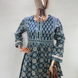 May include: A blue tunic with a floral pattern is displayed on a mannequin. The tunic has long sleeves, a round neckline, and a flared hem. The pattern includes white and teal accents. The cuffs and neckline are trimmed with white lace.