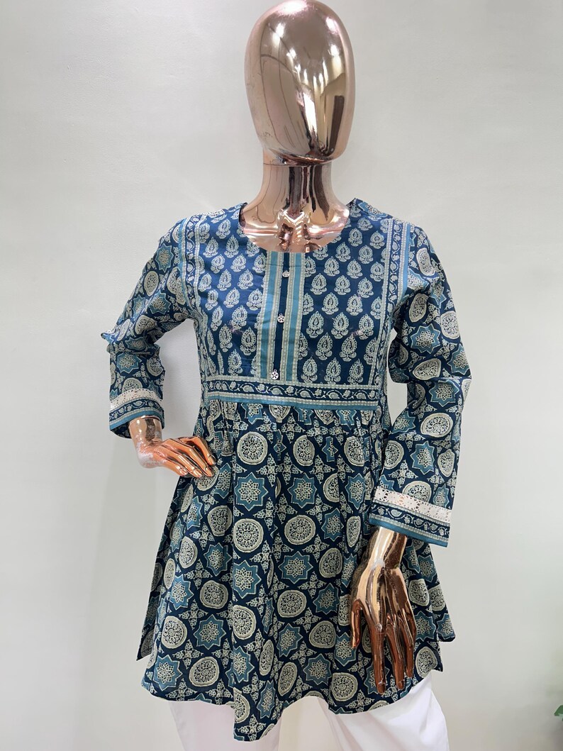 May include: A blue tunic with a floral pattern is displayed on a mannequin. The tunic has long sleeves, a round neckline, and a flared hem. The pattern includes white and teal accents. The cuffs and neckline are trimmed with white lace.