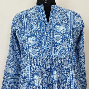 May include: A blue and white floral print long-sleeved tunic with a V-neck and a beaded trim. The tunic has a gathered waist and a relaxed fit.