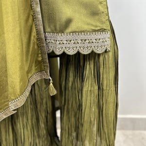 May include: Olive green palazzo pants with a lace trim and a pleated design. The pants have a tassel detail on the side.