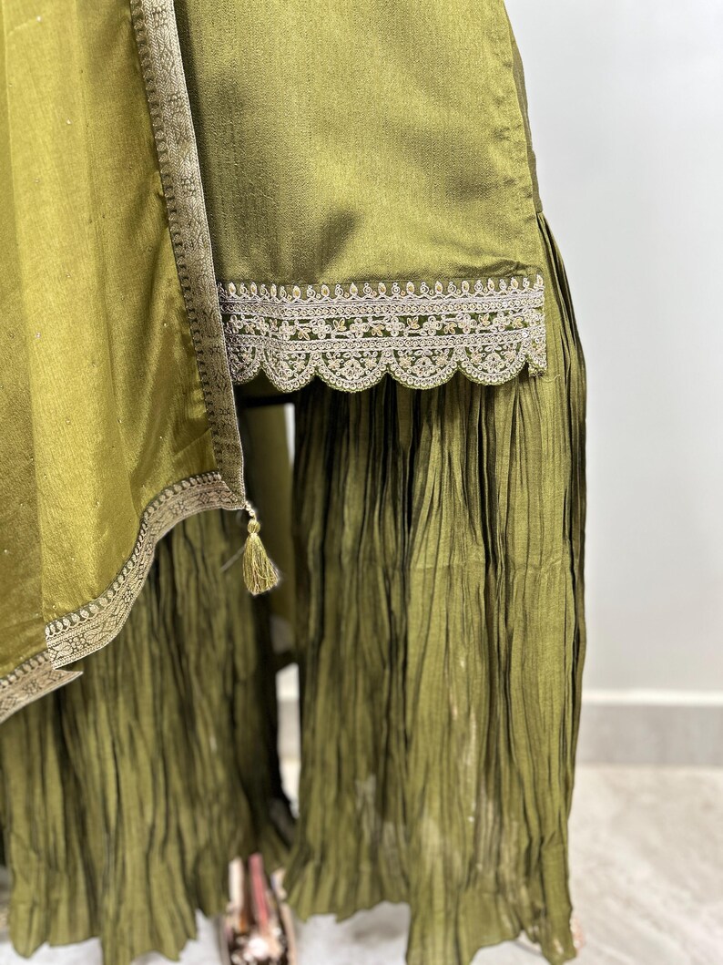 May include: Olive green palazzo pants with a lace trim and a pleated design. The pants have a tassel detail on the side.