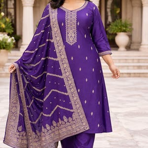 May include: A striking purple salwar kameez outfit. The set includes a tunic top, trousers, and a dupatta. Gold embroidery details the neckline, sleeves, and dupatta edge. The fabric has a gentle sheen, and the outfit is suitable for special events.