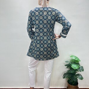 May include: A long-sleeved tunic and white pants ensemble. The tunic features a dark blue and light blue geometric pattern. The white pants have a decorative hem. The outfit is displayed on a mannequin.